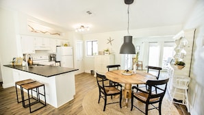 A modern kitchen with a central island, wooden chairs, and a hanging light fixture.