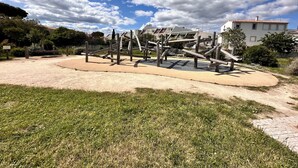 Ein Spielplatz mit Klettergerüsten und Sandbereich, umgeben von Gras und einem Gebäude im Hintergrund.