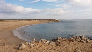 Una platja sorrenca amb una roca prominent al primer pla i un mar tranquil.