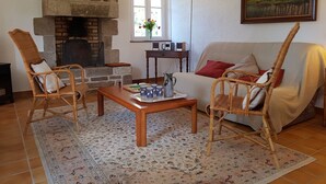 Un saló d'estar acollidor amb una llar de pedra, mobles de vimetes, una catifa amb dibuixos i un quadre a la paret.