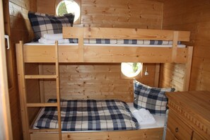 Ein Schlafraum mit Etagenbetten, Holzvertäfelung, einem kleinen Fenster und einer Kommode.