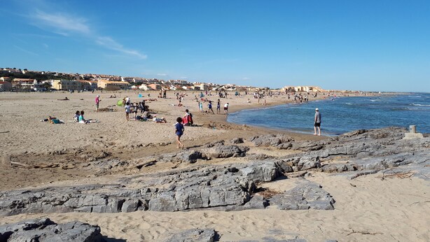 A beach with rocky foreground, people sunbathing, and buildings in the background. - COMFORTABLE SEA-FRONT PAVILION (Fleury)