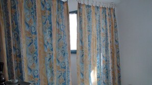 A room with patterned curtains, a table with a bowl of fruit, and a window. - COMFORTABLE SEA-FRONT PAVILION (Fleury)