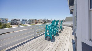 A wooden deck with chairs, a white railing, and a view of houses in the background. - 5454- Sea View - Nags Head Semi-Oceanfront | Private Pool (Nags Head)