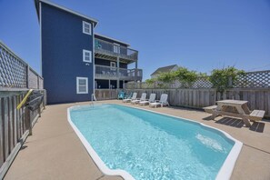 A swimming pool with lounge chairs and a wooden deck, surrounded by a wooden fence and a two-story building.