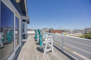 Une terrasse en bois avec des chaises blanches et turquoise, une vue sur la plage et un bâtiment doté de grandes fenêtres.