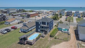 A coastal residential area with a large building featuring a pool, a pier, and a view of the ocean. - 5454- Sea View - Nags Head Semi-Oceanfront | Private Pool (Nags Head)