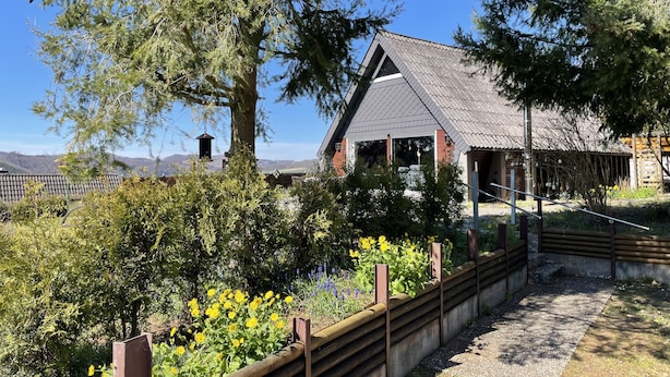 A rustic building with a sloped roof, surrounded by dense greenery and a wooden fence. - Quiet, cozy vacation home with fireplace, barbecue area and fantastic views (Hatzfeld (Eder))