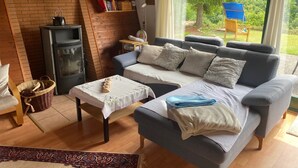 A cozy living room with a sofa, a small table, a fireplace, and a view of greenery outside. - Quiet, cozy vacation home with fireplace, barbecue area and fantastic views (Hatzfeld (Eder))