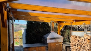 An outdoor barbecue area with a covered roof, a brick oven, and a stack of firewood. - Quiet, cozy vacation home with fireplace, barbecue area and fantastic views (Hatzfeld (Eder))