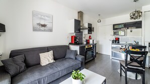 Ein modernes Wohnzimmer mit grauem Sofa, einem weißen Couchtisch mit Pflanze und einem Essbereich mit schwarzem Stuhl.