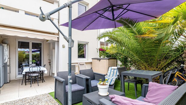 An outdoor patio with wicker furniture, a table, and a purple umbrella.