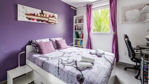 Ein Schlafzimmer mit einem Bett, einem Schreibtisch, einem Stuhl, einem Bücherregal und einem Fenster mit Vorhängen.