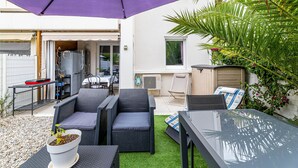 Ein Patio im Freien mit Esstisch, Stühlen, einem violetten Sonnenschirm und einem kleinen Garten.