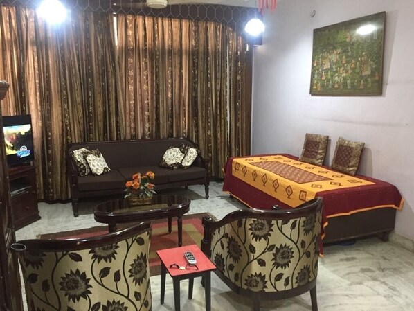 A room with a sofa, a bed with a patterned bedspread, a coffee table, and floral-patterned armchairs.