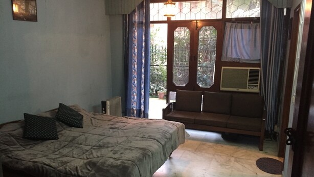 Un dormitori amb llit, sofà, radiador i finestra amb cortines.