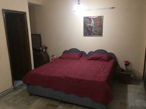 A bedroom with a bed, a door, a wall-mounted artwork, and a small table with a vase.