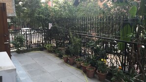 Un pati amb un paviment de rajoles, plantes en testos, una tanca de metall negre i una mànega de jardí groga.