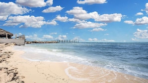 A beach with a thatched-roof structure, a pier extending into the sea, and footprints in the sand. - Key Colony Beach Waterfront 6BR w/ Pool & Dock (Key Colony Beach)