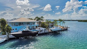 A waterfront property with a dock, boats, and a house with a balcony overlooking the water. - Key Colony Beach Waterfront 6BR w/ Pool & Dock (Key Colony Beach)