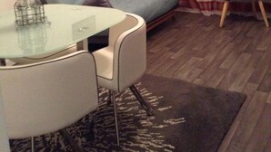 Ein kleines, gemütliches Wohnzimmer mit einem blauen Sofa, einem Glastisch und einem dunklen Teppich.