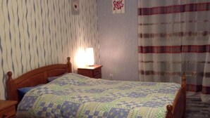 Ein Schlafzimmer mit einem hölzernen Bett, einem Nachttisch, einer Lampe, strukturierten Tapeten und einem karierten Boden.