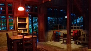 A cozy indoor space with a wooden table and chairs, a bookshelf, and a view of greenery outside. - Beachfront-rainforest tropical paradise retreat, Drake Bay, Osa Peninsula (Bahia Drake)