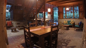 A rustic wooden interior with a dining area, seating, and large windows offering views of greenery. - Beachfront-rainforest tropical paradise retreat, Drake Bay, Osa Peninsula (Bahia Drake)