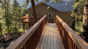 Une terrasse en bois qui mène à une maison entourée d’arbres et de montagnes.