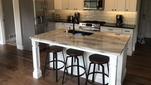 Une cuisine moderne avec des meubles blancs, un réfrigérateur en acier inoxydable, un four à micro-ondes, une cuisinière et un îlot en marbre agrémenté de tabourets de bar.