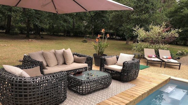 Un área junto a la piscina con mobiliario de mimbre, una terraza de madera y una piscina.