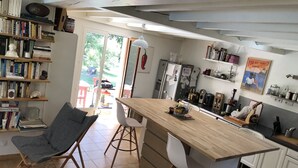 Una cocina moderna con una isla de madera, sillas blancas y una estantería llena de libros.