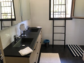 Een moderne badkamer met een zwart aanrecht, een spiegel, twee wastafels, een handdoek, een prullenbak, een zwarte ladder en een gestreept tapijt.