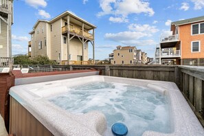Een bubbelbadgedeelte met houten leuningen, een houten terras en een uitzicht op meerverdieping hoge gebouwen op de achtergrond.