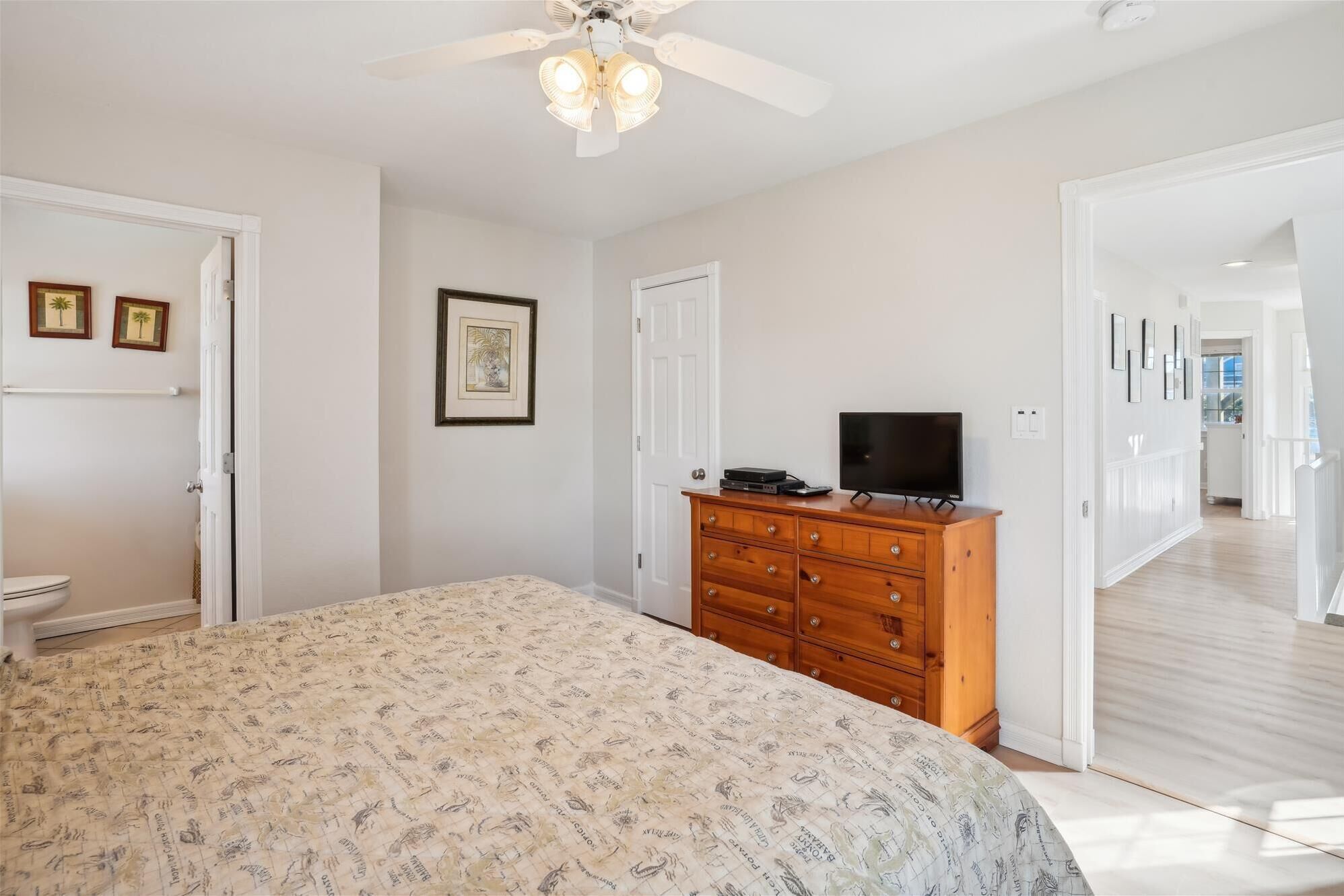 A bedroom with a bed, dresser, TV, and a hallway leading to another room.