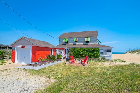 A two-story house with a red garage and a covered patio area with red chairs.