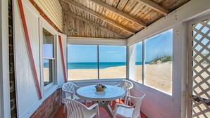 A covered patio with a table and chairs, overlooking a beach. - 5452- Sea Captain's Cottage - Historic Oceanfront Cottage | Nags Head (Nags Head)