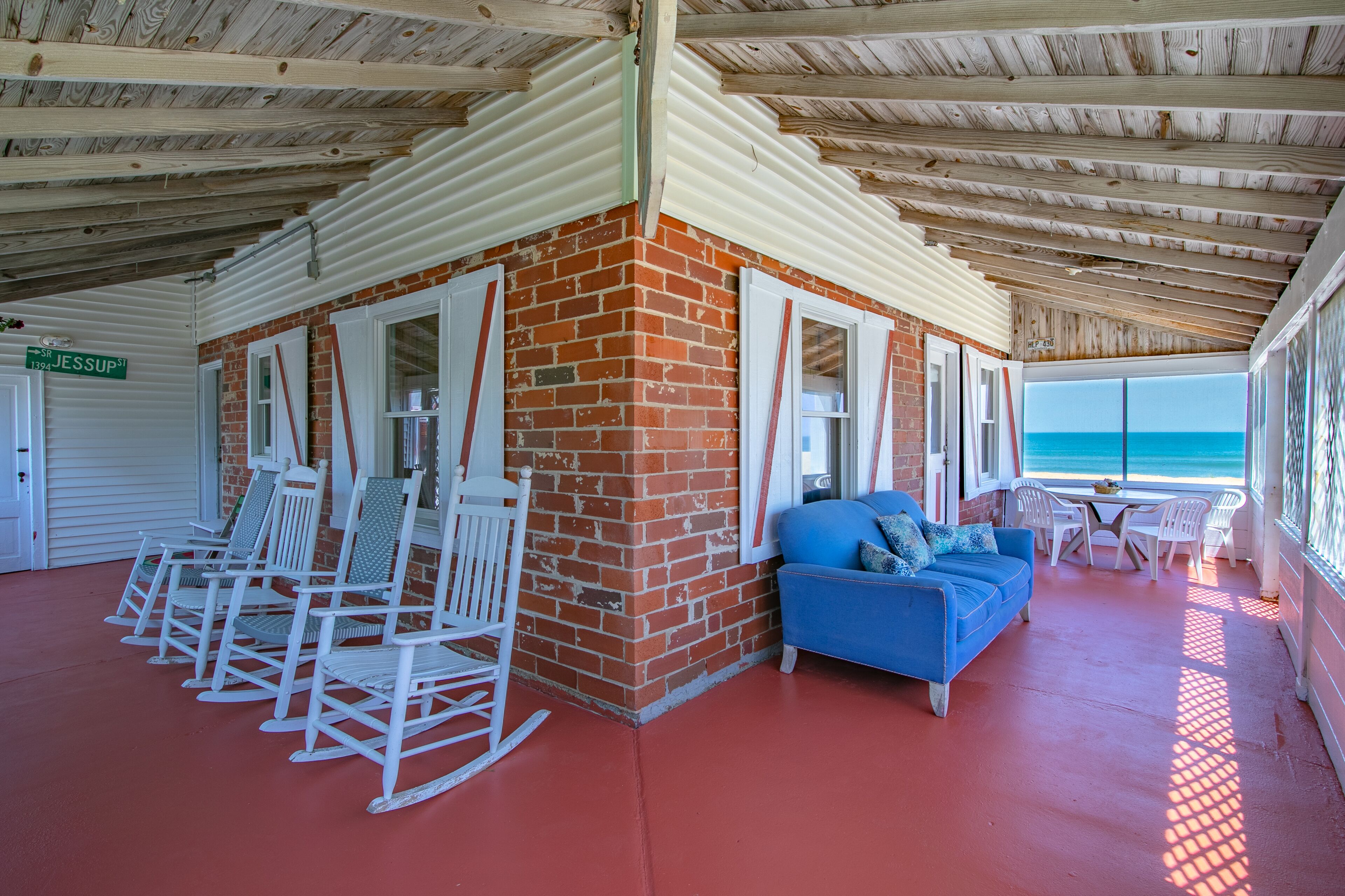 A covered outdoor area with a brick wall, white rocking chairs, a blue sofa, and a table with chairs.