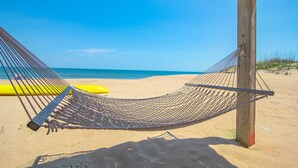A hammock on a sandy beach with a clear blue sky and ocean in the background. - 5452- Sea Captain's Cottage - Historic Oceanfront Cottage | Nags Head (Nags Head)