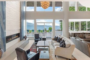 A spacious living area with a fireplace, comfortable seating, and large windows offering a view of the sea. - Sleeps 24! Luxe Waterfront Estate w Beach, Hot Tub (Sagle)