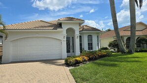 A residential house with a white garage, a tiled roof, and a well-maintained lawn with various plants. - Stunning Naples home with pool, bike to the Gulf at Wiggins or Vanderbilt.  (Naples)