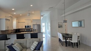 A modern kitchen with white cabinets, a central island, and a dining area with a table and chairs. - Stunning Naples home with pool, bike to the Gulf at Wiggins or Vanderbilt.  (Naples)