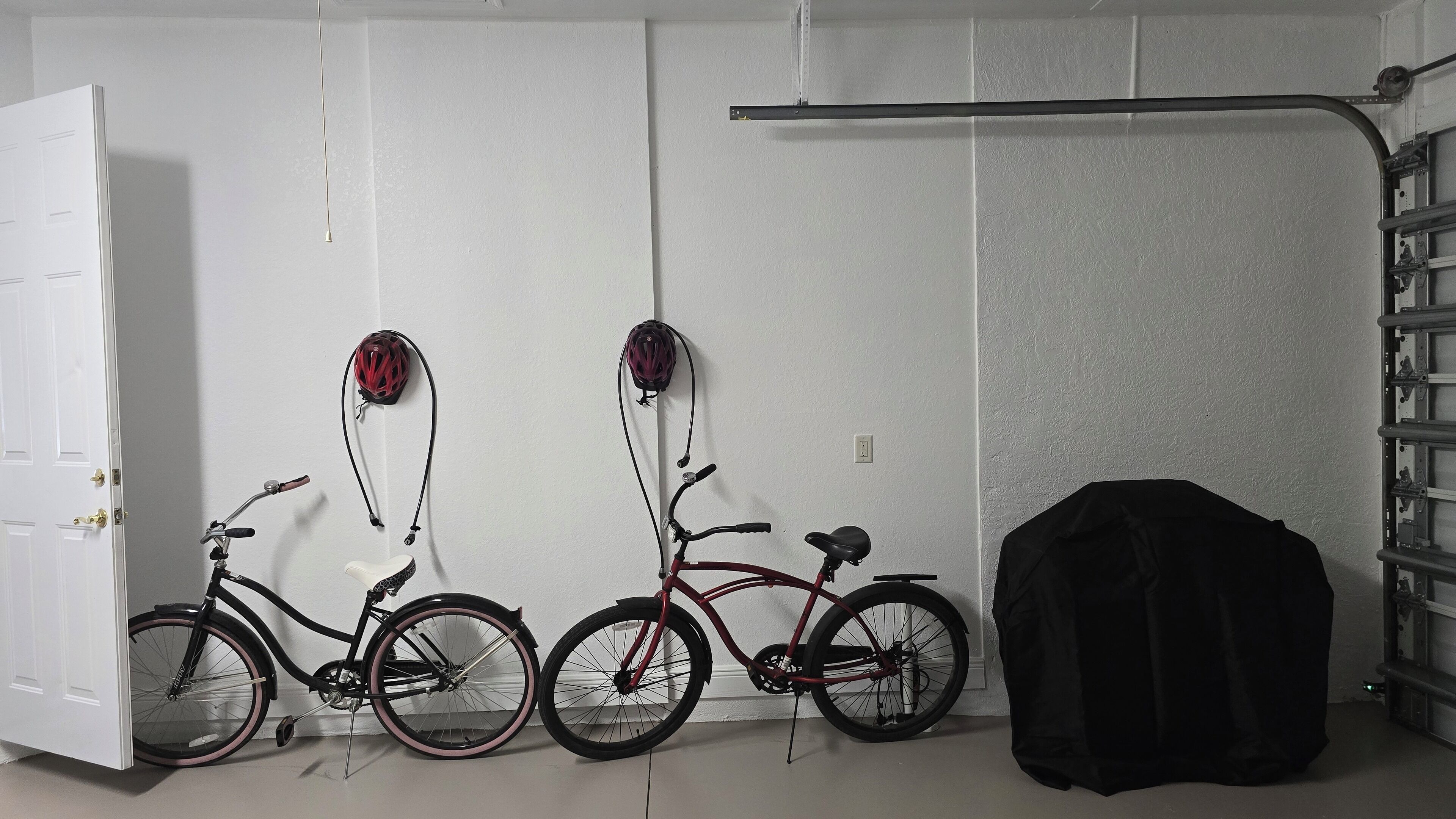 Quarto com duas bicicletas, uma porta, um cabideiro e uma mala preta.