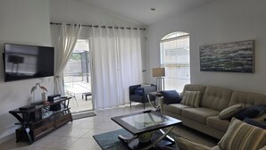 A living room with a TV, a sofa, a coffee table, and a window with curtains. - Stunning Naples home with pool, bike to the Gulf at Wiggins or Vanderbilt.  (Naples)