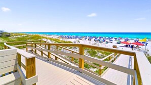 Un pontile in legno con vista su una spiaggia, ombrelloni e persone.