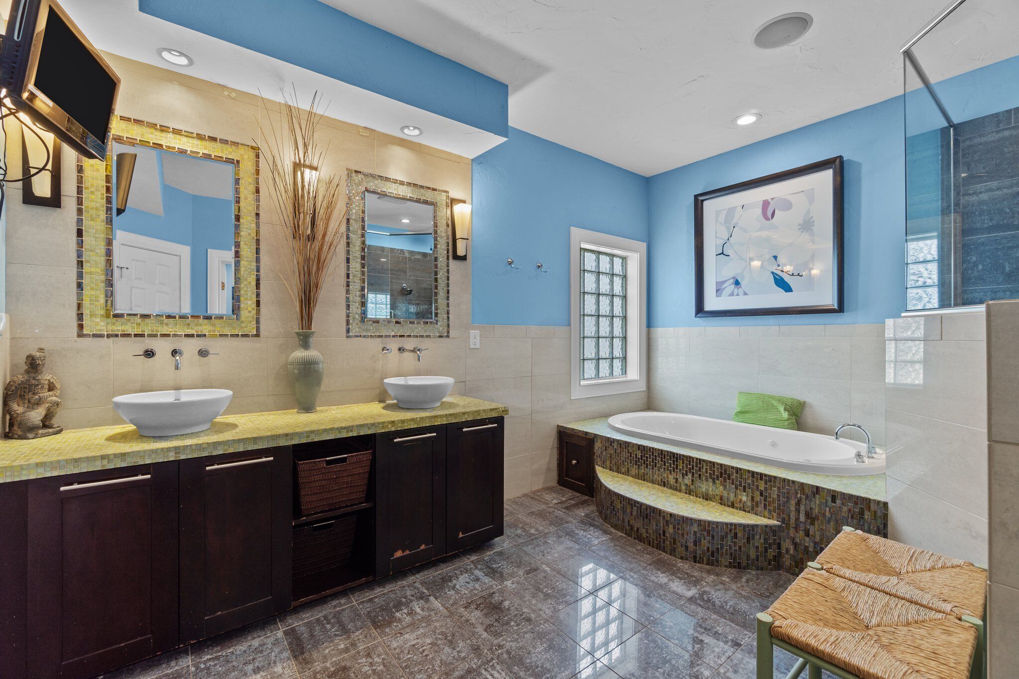 A modern bathroom with two sinks, a large bathtub, and a mirror with mosaic tiles.
