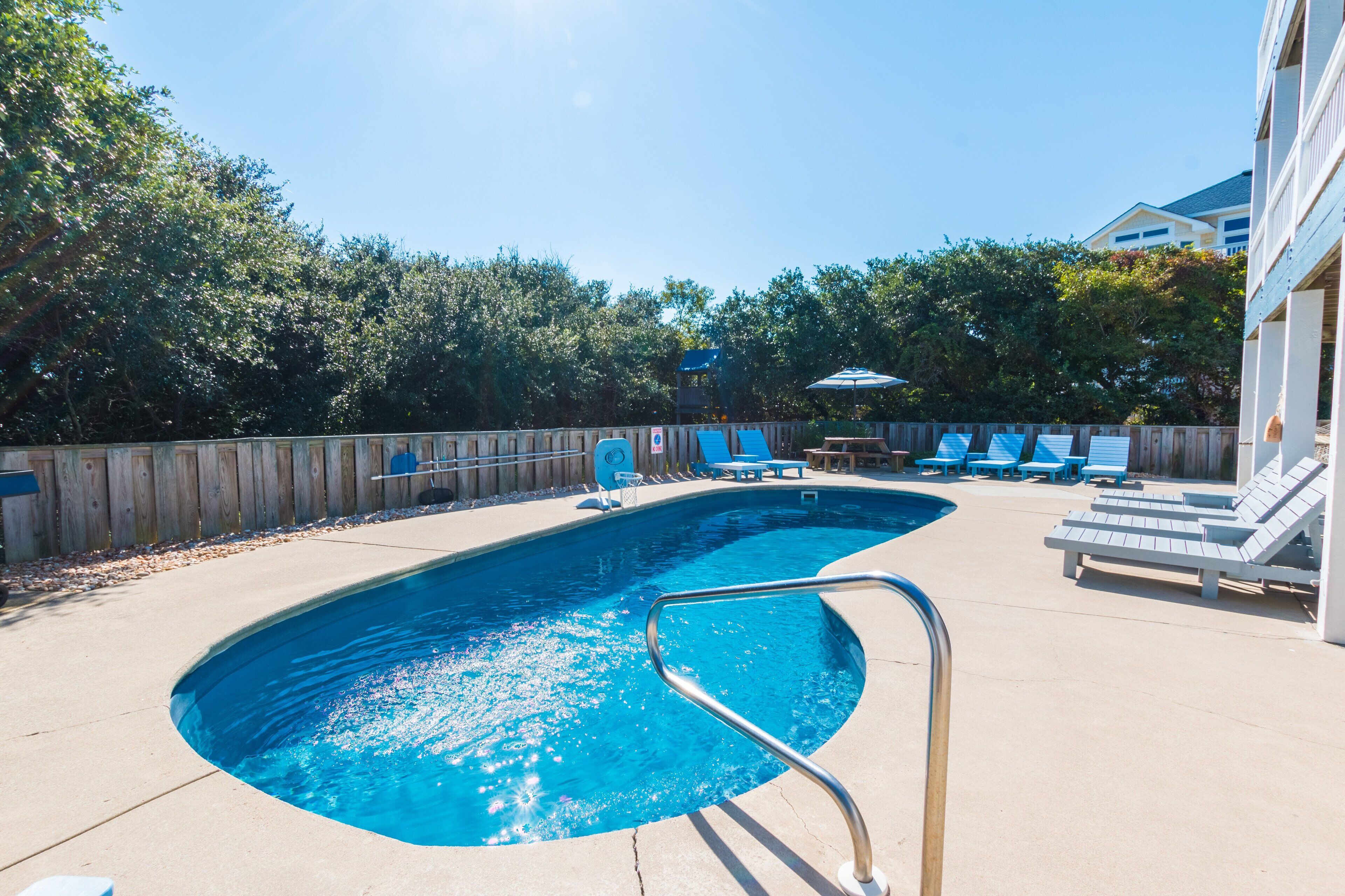 A swimming pool with a wooden deck, lounge chairs, and a wooden fence.