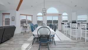 A spacious dining area with a high ceiling, large windows, and a view of the outdoors. - 2310 - Aegean Breeze, Corolla Estate w/ Heated Pool, Spa & Billiards (Corolla)