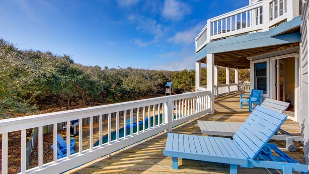 A wooden deck with blue lounge chairs, a pool, and a white railing overlooking a natural landscape. - 2310 - Aegean Breeze, Corolla Estate w/ Heated Pool, Spa & Billiards (Corolla)