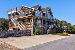 Une maison à plusieurs étages dotée d’une terrasse en bois, de plusieurs balcons et d’un escalier menant aux niveaux supérieurs.
